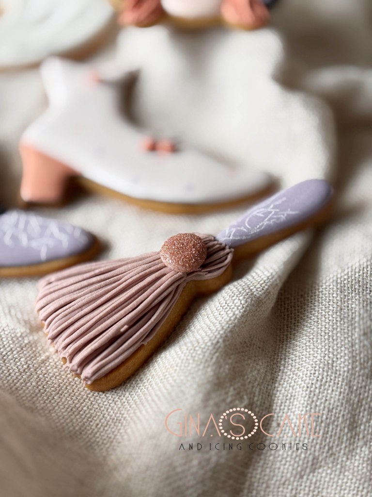 Biscotti decorati a forma di scarpette e un pennello, con glasse colorate su uno sfondo di tessuto chiaro.