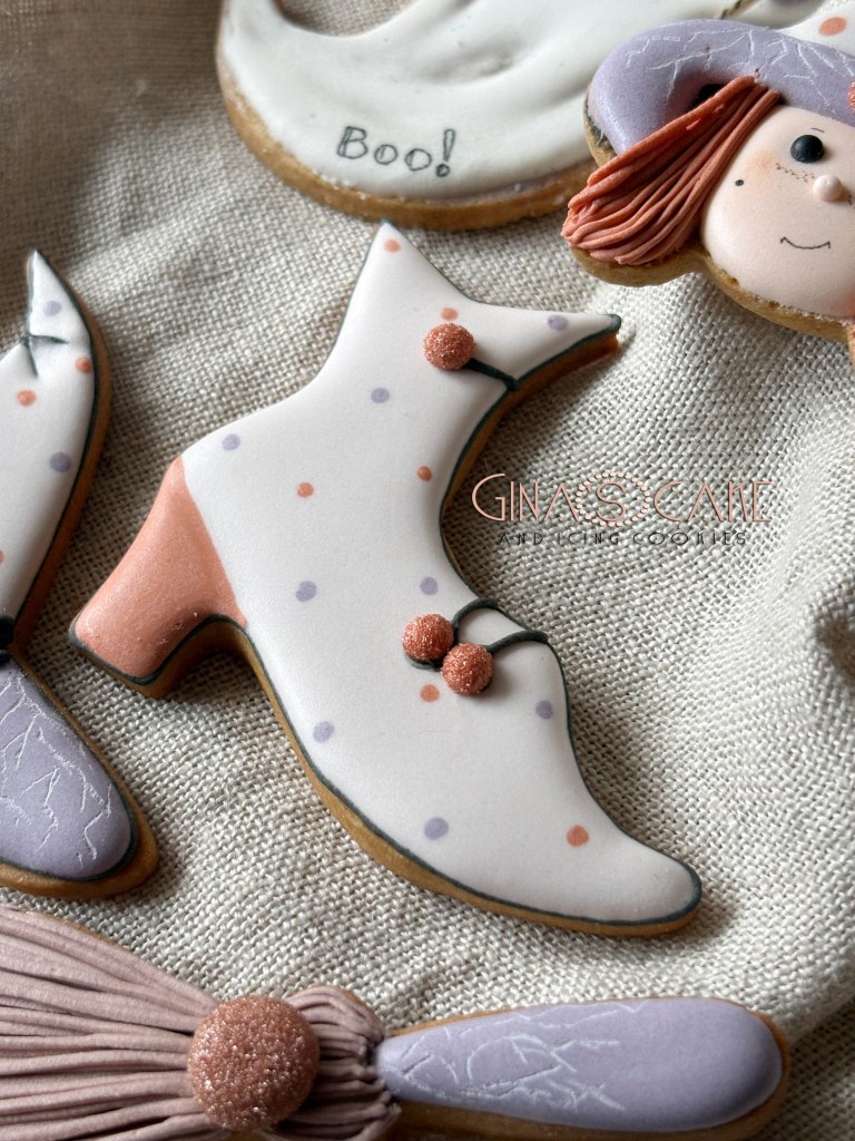 Biscotti decorati a forma di scarpa, con dettagli colorati e palline, su uno sfondo di tessuto beige.