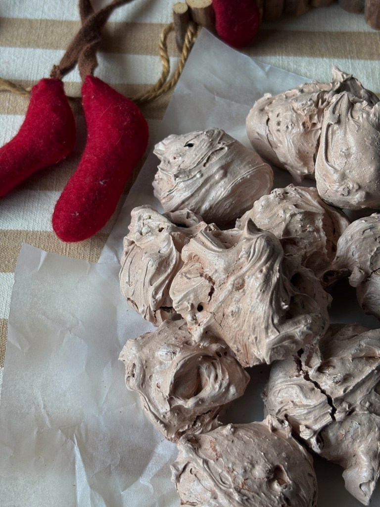 Meringhe al cioccolato su carta da forno con decorazioni natalizie in sfondo.