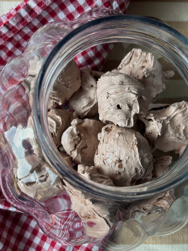 Vaso di vetro contenente cioccolato fuso montato, su un tavolo con tovagliolo a quadretti rossi e bianchi.