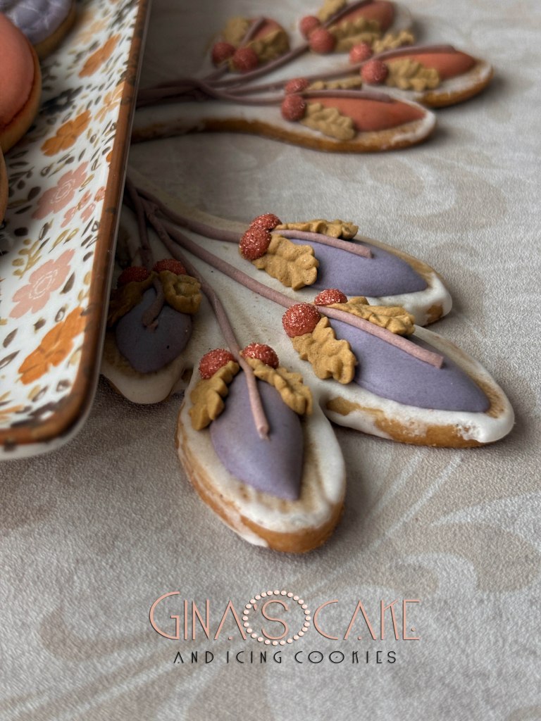 Biscotti decorati con glassa in forme di foglie e fiori, presentati su un piatto elegante.