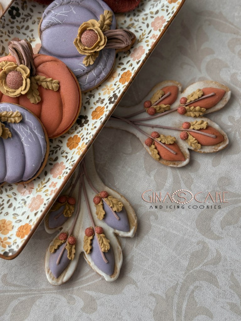 Piatto decorato con biscotti a forma di zucche colorate e fiori, su un tovagliolo elegante.