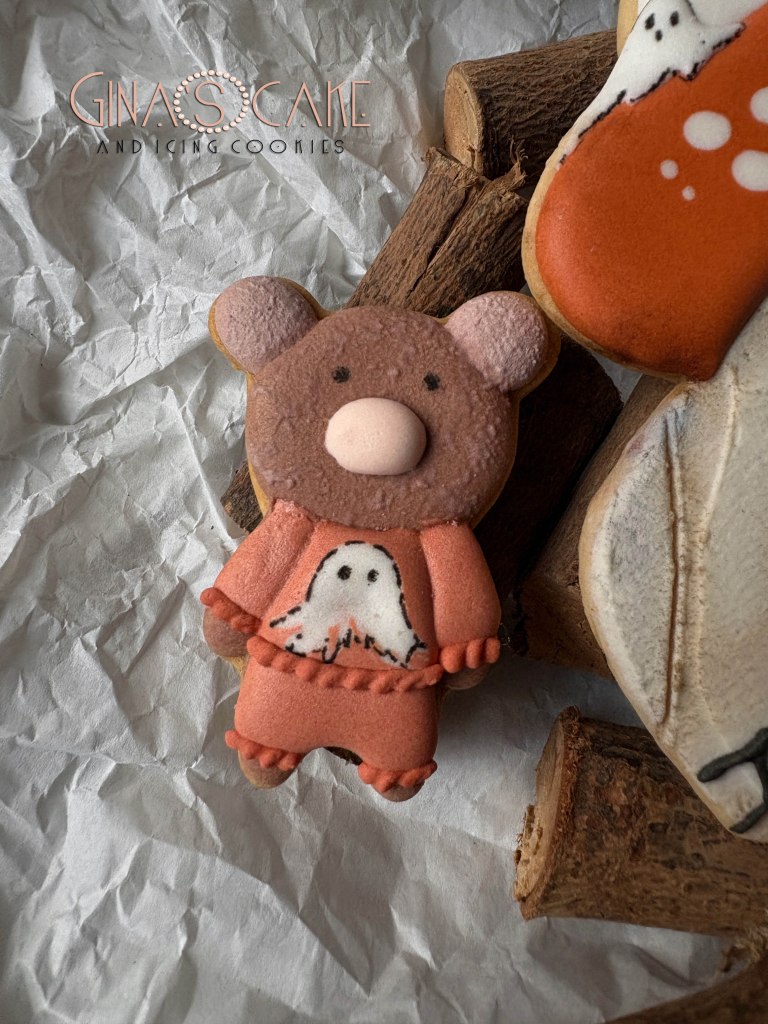 Biscotto decorato a forma di orsetto con un fantasma, su sfondo di legno e carta stracciata.